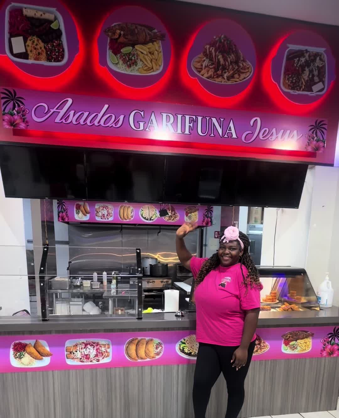 Mostrador de Asados Garífuna Jesús con letrero rosa luminoso y una integrante del equipo saludando